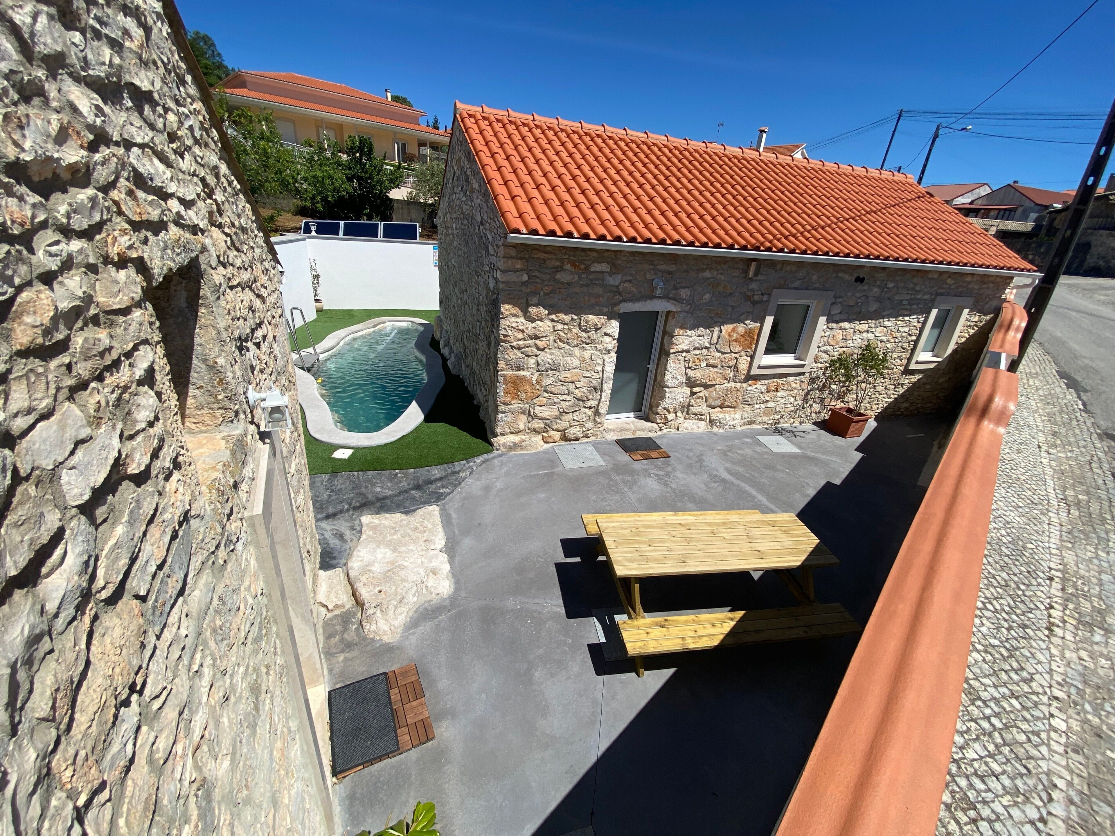 Un bâtiment en pierre avec un toit recouvert de tuiles rouges, une piscine et une table en bois.