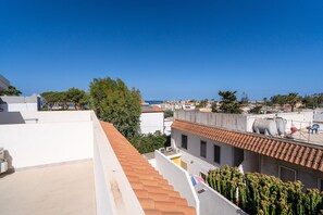 A rooftop terrace with a view of the city, a cactus plant, and a red-tiled roof.