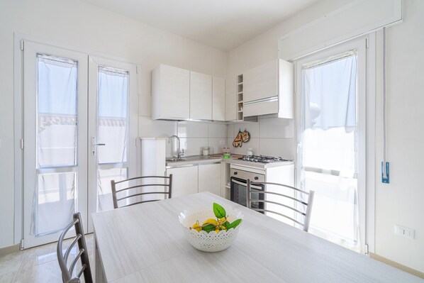 A modern kitchen with white cabinets, a dining table with chairs, and a window with curtains.