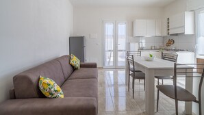 Una cocina moderna con armarios blancos, una mesa de comedor con sillas y un sofá con un cojín floral.