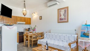 A living room with a sofa, a dining table, chairs, a TV, and a kitchen area with cabinets and appliances. - Apartment 'Agnadi' with Sea View, Balcony and Air Conditioning (Serifos)