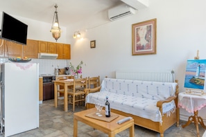 A living room with a sofa, a dining table, chairs, a TV, and a kitchen area with cabinets and appliances.