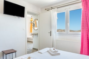A hotel room with a bed, a television mounted on the wall, a window with curtains, and a bathroom visible through an open door.