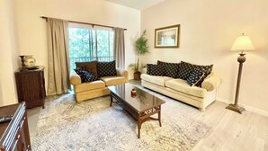 A living room with a sofa, a coffee table, a lamp, a plant, and a window with curtains. - Charming Villa at Bahama Bay (Davenport)