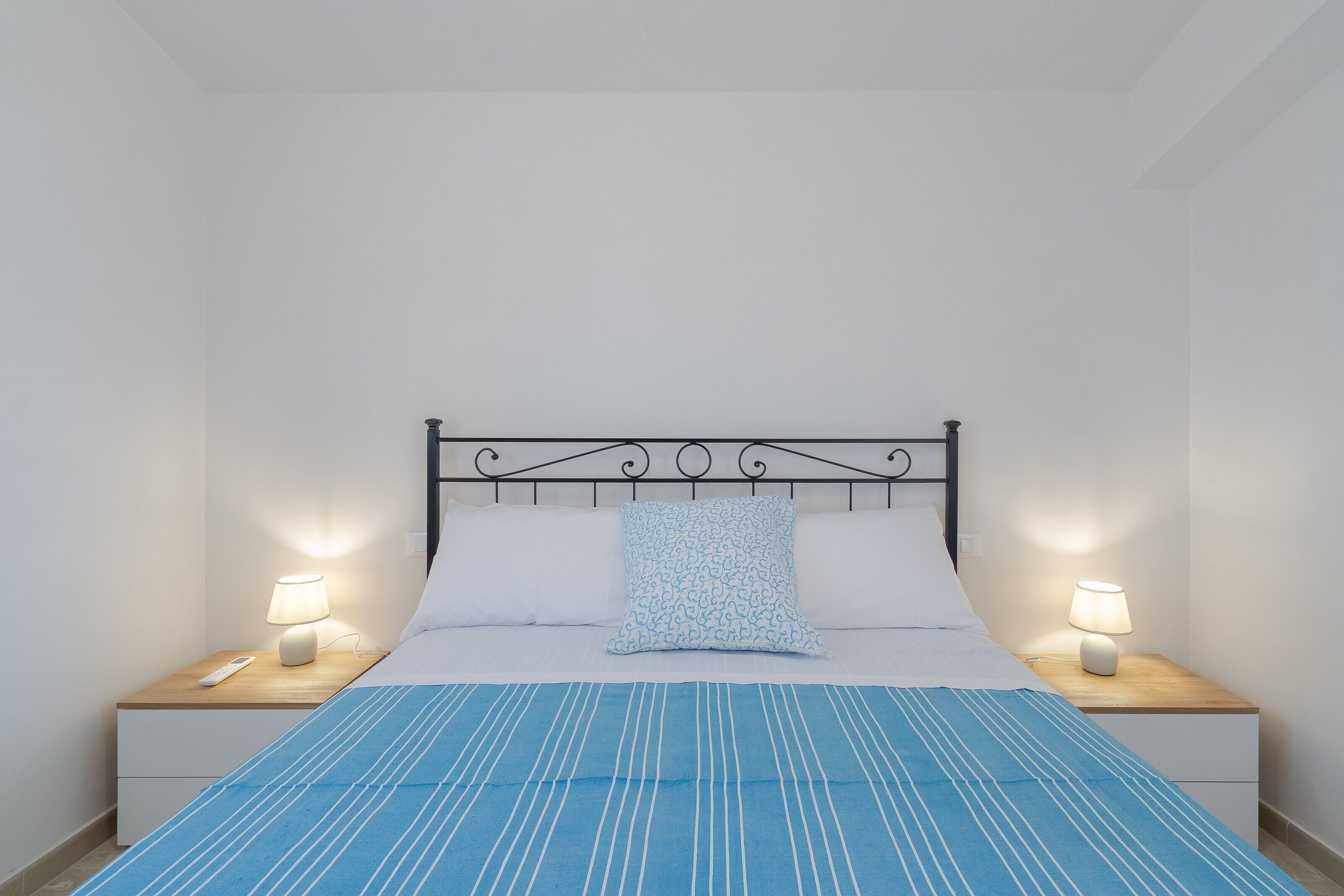 A neatly made bed with a blue-striped bedspread, two bedside lamps, and a patterned pillow.