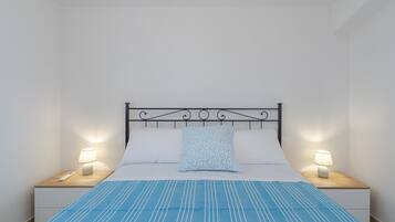 A neatly made bed with a blue-striped bedspread, two bedside lamps, and a patterned pillow.
