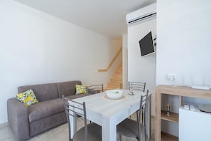 A modern living room with a sofa, dining table, chairs, a staircase, and a mounted TV. - Apartment 'Appartamento Nautilus' with Sea View, Wi-Fi and Air Conditioning (Marzamemi)