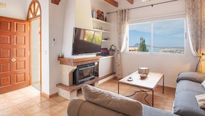 A living room with a fireplace, television, sofa, and a window with a view. - Holiday Home 'Chalet Altea' with Sea View, Wi-Fi and Air Conditioning (Altea)