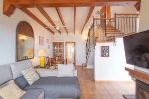 A living room with a sofa, a television, a fireplace, a staircase, and a dining area. - Holiday Home 'Chalet Altea' with Sea View, Wi-Fi and Air Conditioning (Altea)