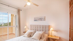A bedroom with a bed, two bedside lamps, a ceiling fan, a painting, and a view through a sliding door. - Holiday Home 'Chalet Altea' with Sea View, Wi-Fi and Air Conditioning (Altea)