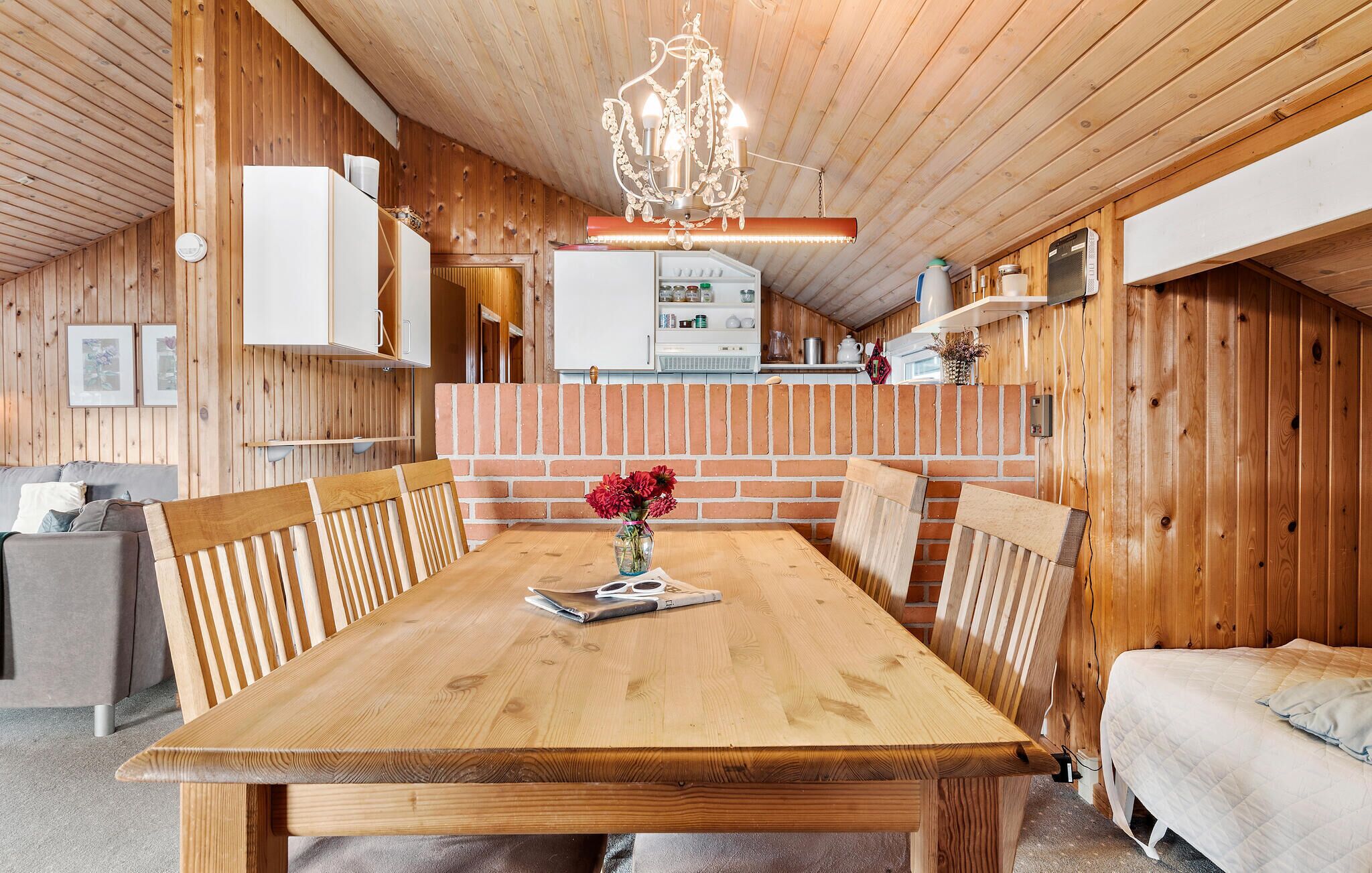 A wooden interior with a dining table, chairs, a chandelier, a fireplace, and a kitchen area.