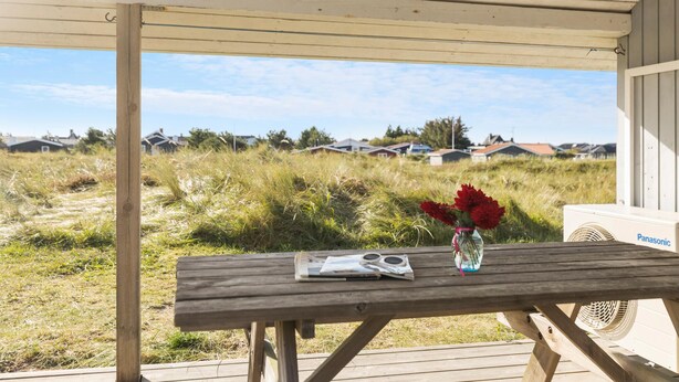 A wooden table with a vase of red flowers and a magazine on a wooden deck. - Pet friendly home in Thisted with sauna (Thisted)