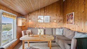 A cozy cabin interior with a wooden ceiling, a sofa, a table with a vase of flowers, and framed pictures on the walls. - Pet friendly home in Thisted with sauna (Thisted)