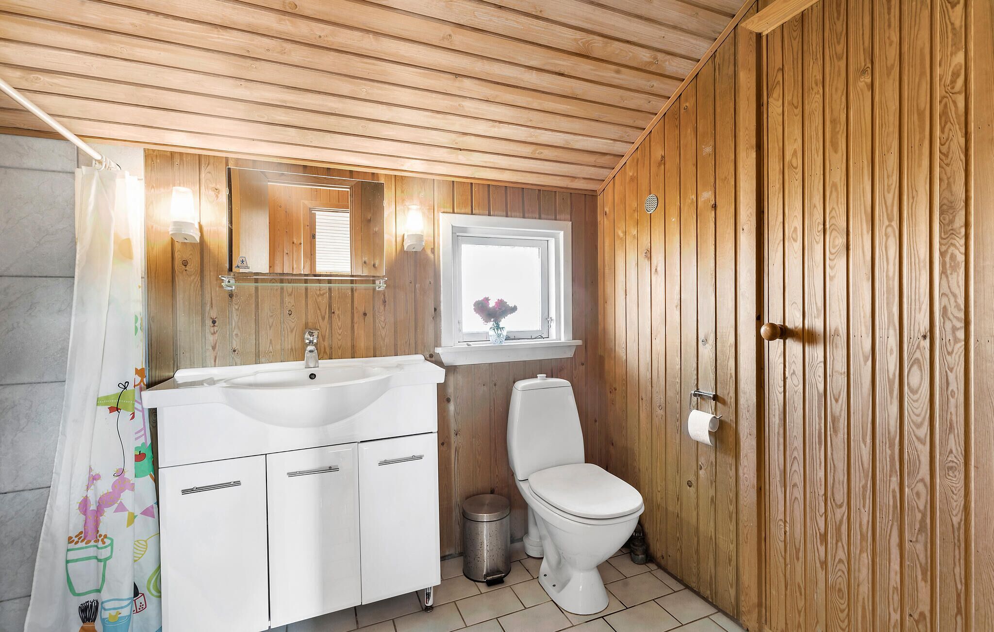 A bathroom with wooden paneling, a white sink, a toilet, and a window with a flower vase.