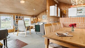 A cozy cabin interior with a wooden ceiling, a dining area with a table and chairs, a kitchen with a brick wall, and a view of the outdoors through a window. - Pet friendly home in Thisted with sauna (Thisted)