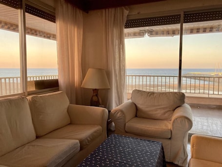 A balcony with a view of the sea, a sofa, a chair, and a table.. Apartment 'En Primera Línea De Mar' with Sea View, Shared Pool and Wi-Fi
