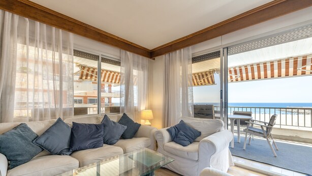 Una sala moderna con una mesa de centro de vidrio, dos sofás con cojines, una lámpara y vista al mar a través de amplios ventanales.
