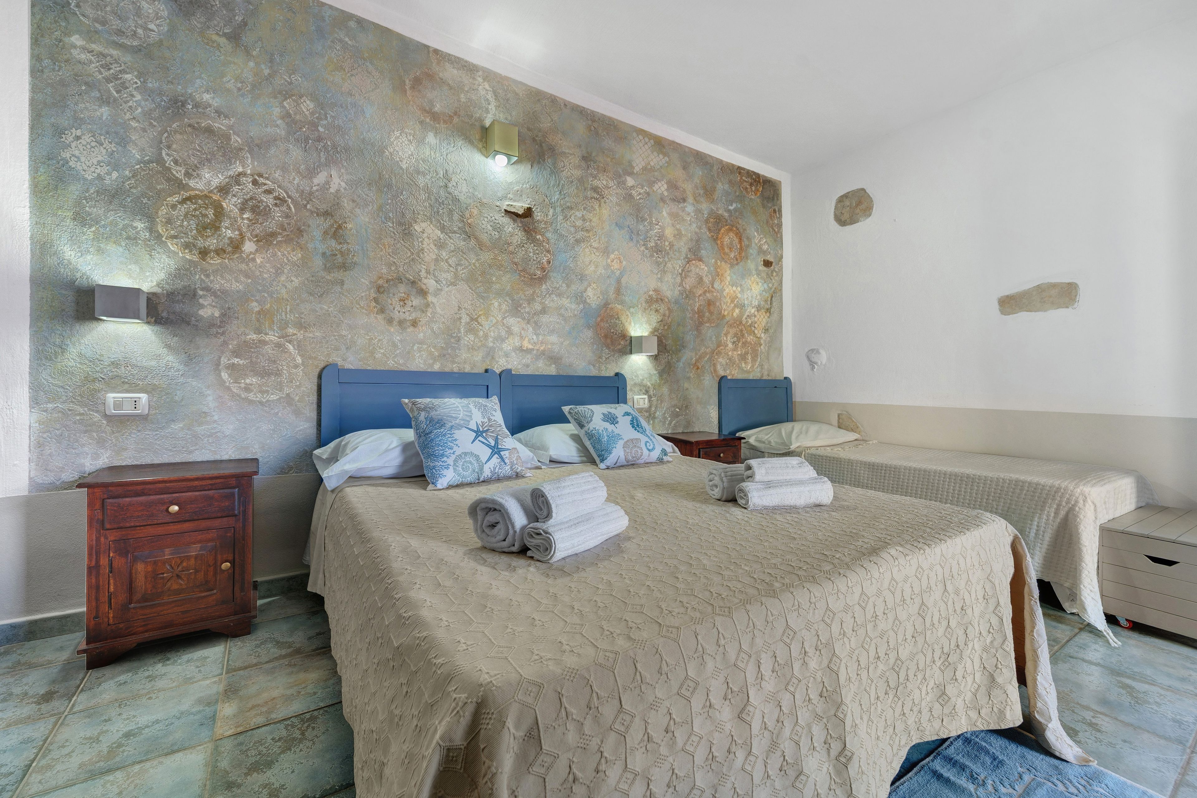 A hotel room with a large bed, two bedside tables, a nightstand, and a wall with a textured mural.