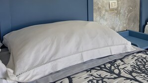 A bedroom with a blue headboard, white bedding, a patterned rug, and a textured wall with a wall-mounted light. - Triple room with shared pool and kitchen, Wi-Fi and air conditioning (Gonnesa)