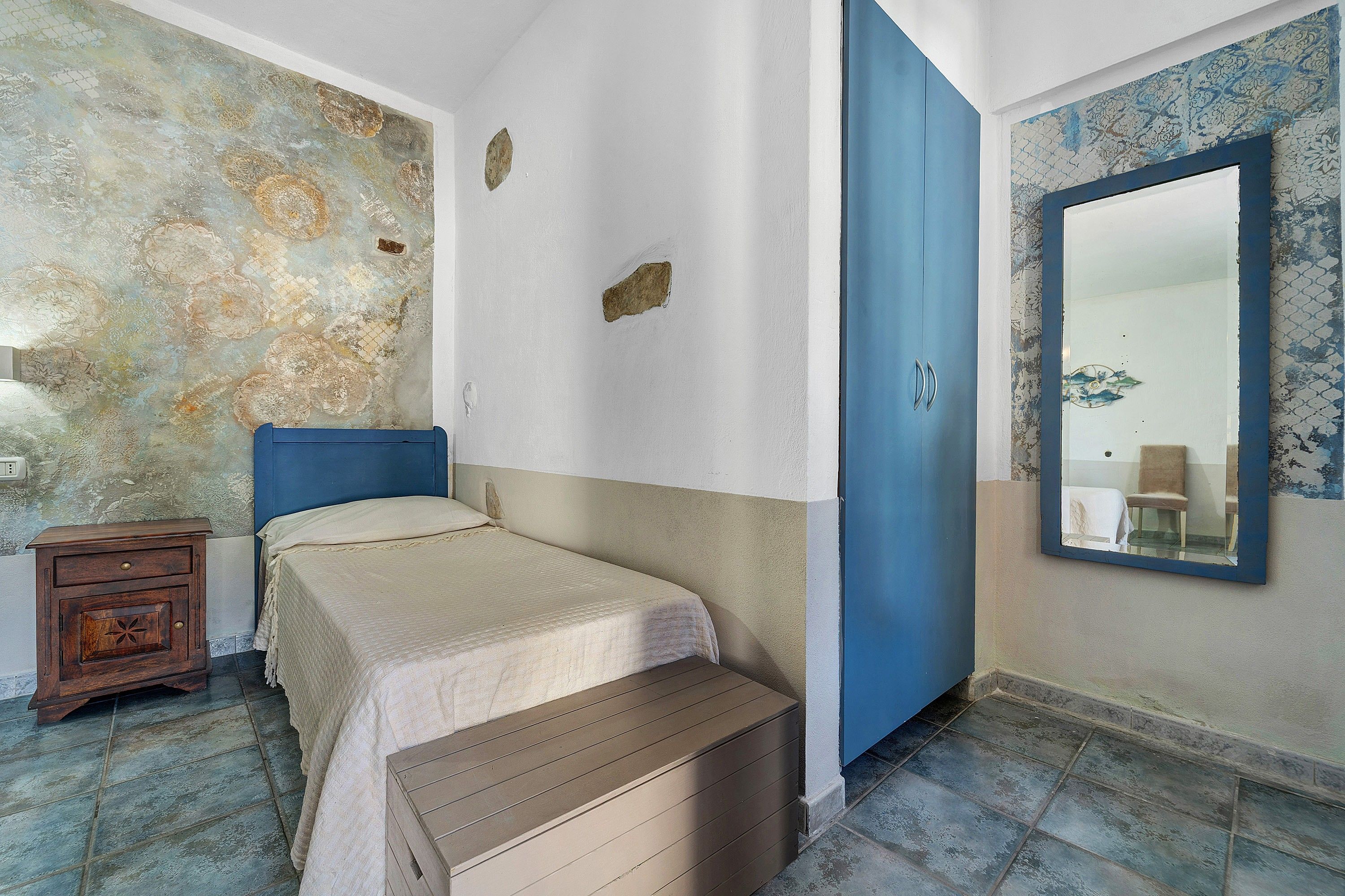 Une pièce comprenant un lit, une commode, un miroir et un mur orné d’un motif décoratif.