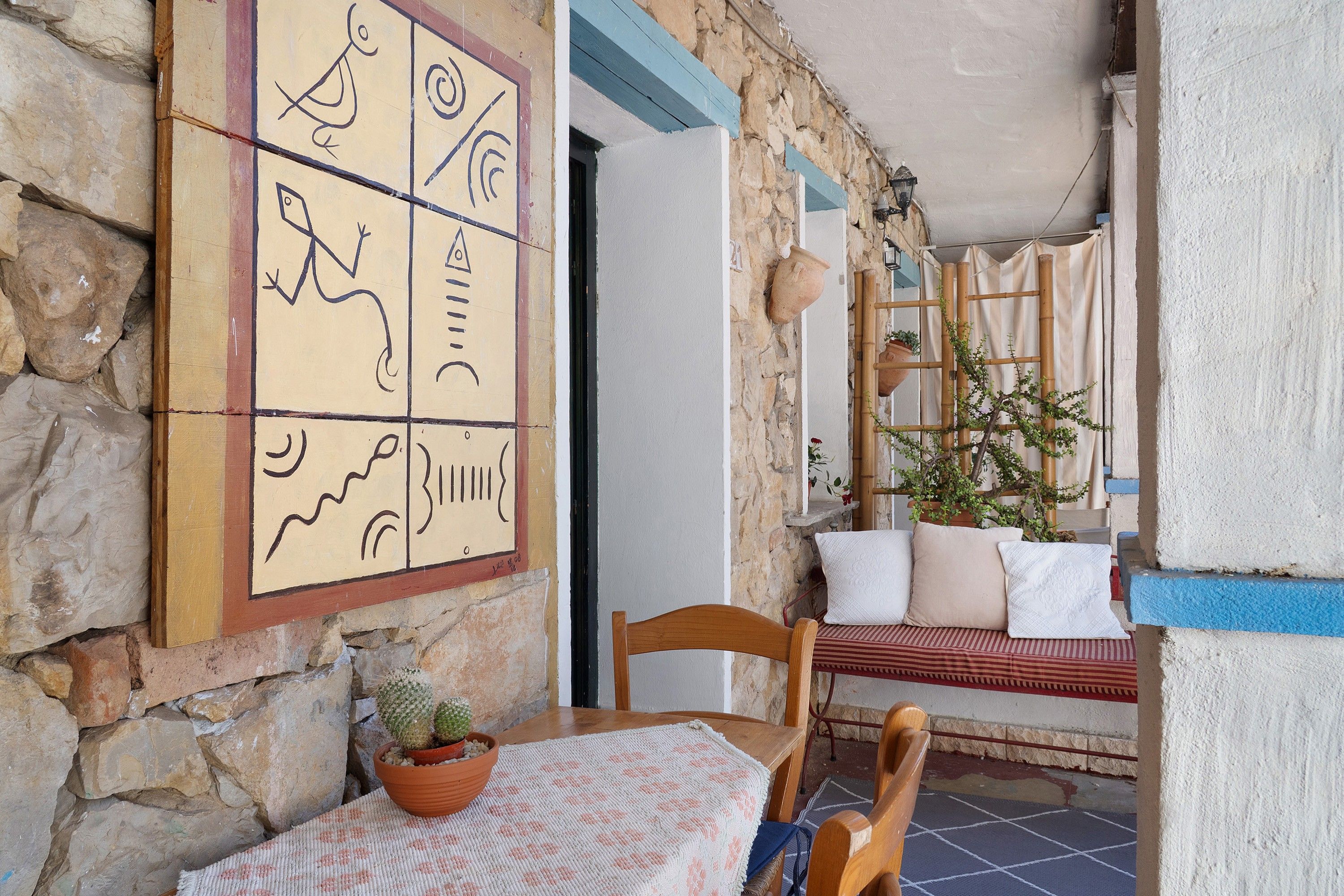 Un muro in pietra con pavimento piastrellato, una sedia di legno, un tavolo con una pianta in vaso e un'opera d'arte appesa al muro.
