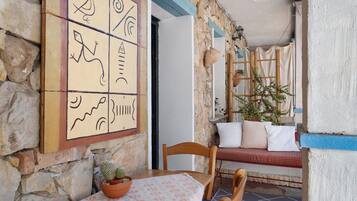 Un muro in pietra con pavimento piastrellato, una sedia di legno, un tavolo con una pianta in vaso e un'opera d'arte appesa al muro.