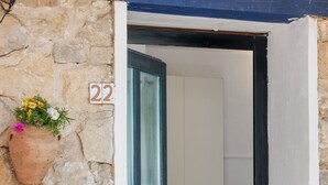 A stone wall with a number plaque, a hanging flower pot, and a doorway leading to a room.