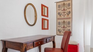A wooden desk with drawers, a red chair, and two framed mirrors on a white wall.