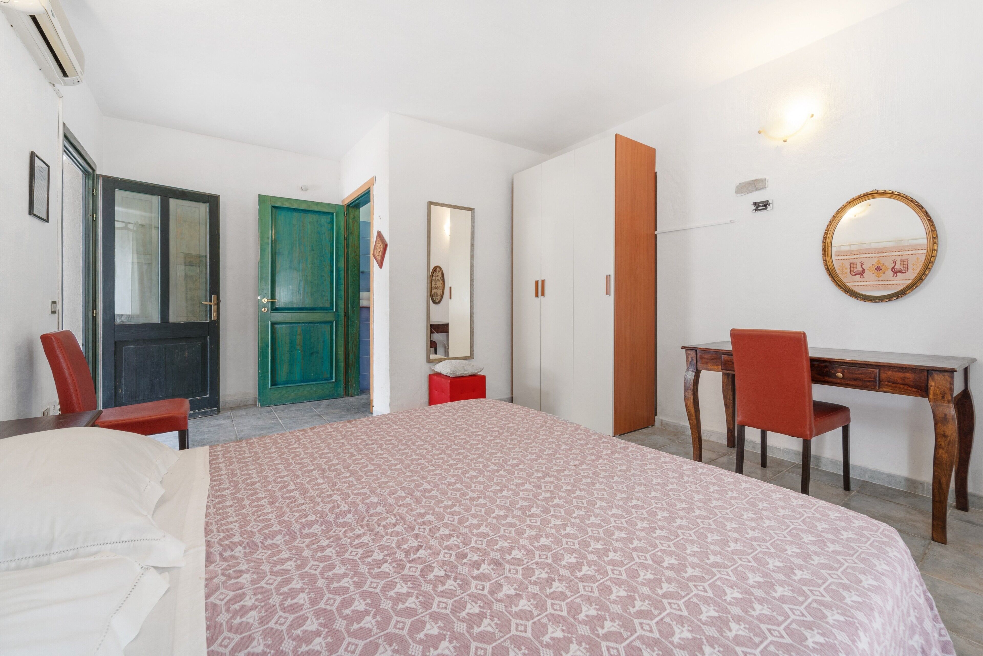 Un dormitorio con cama, escritorio, silla, armario y espejo.