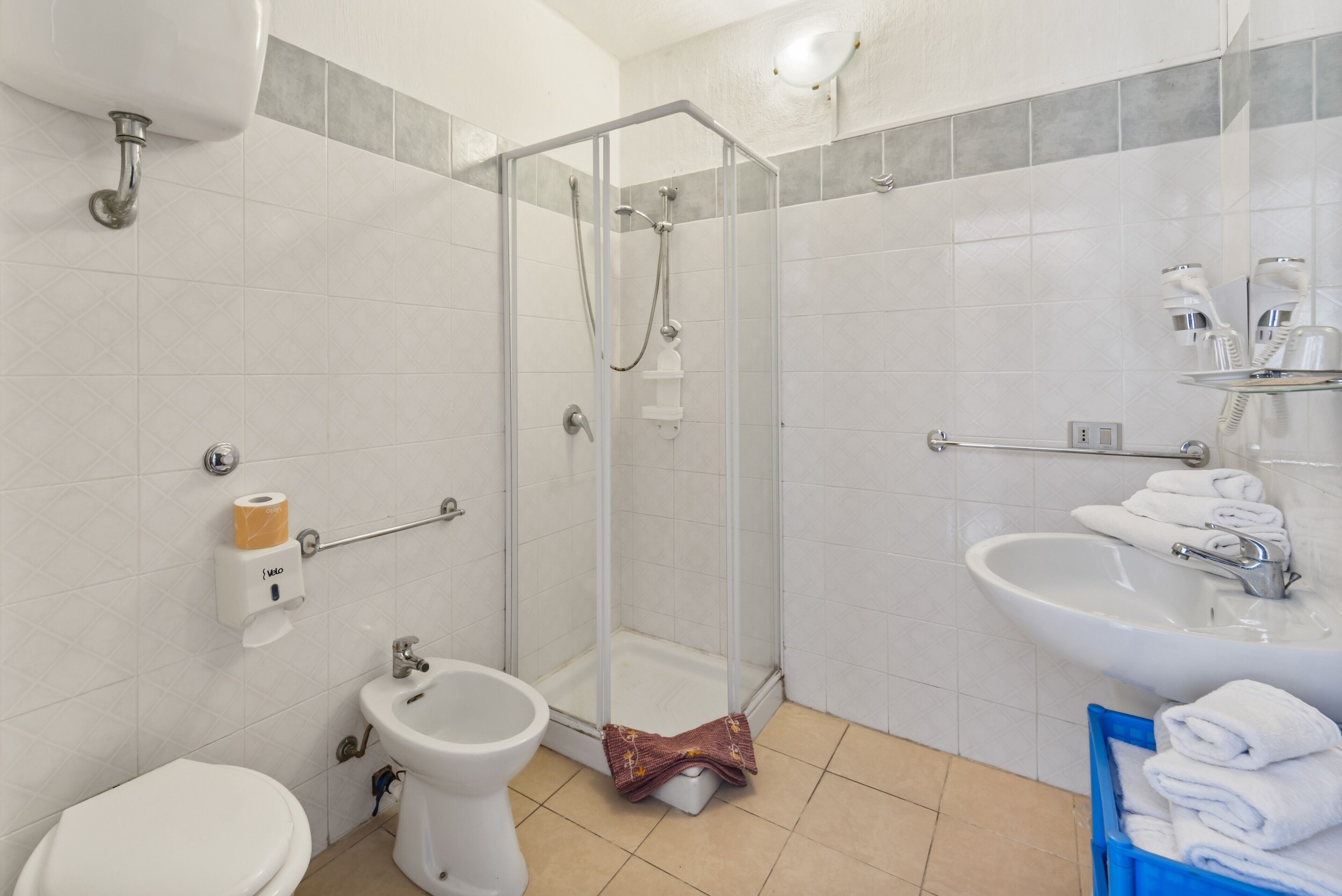 A bathroom with a toilet, bidet, glass shower enclosure, sink, and towel storage.