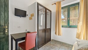 Une pièce comprenant un bureau, une chaise, un téléviseur, une porte-fenêtre coulissante et une fenêtre avec des rideaux.