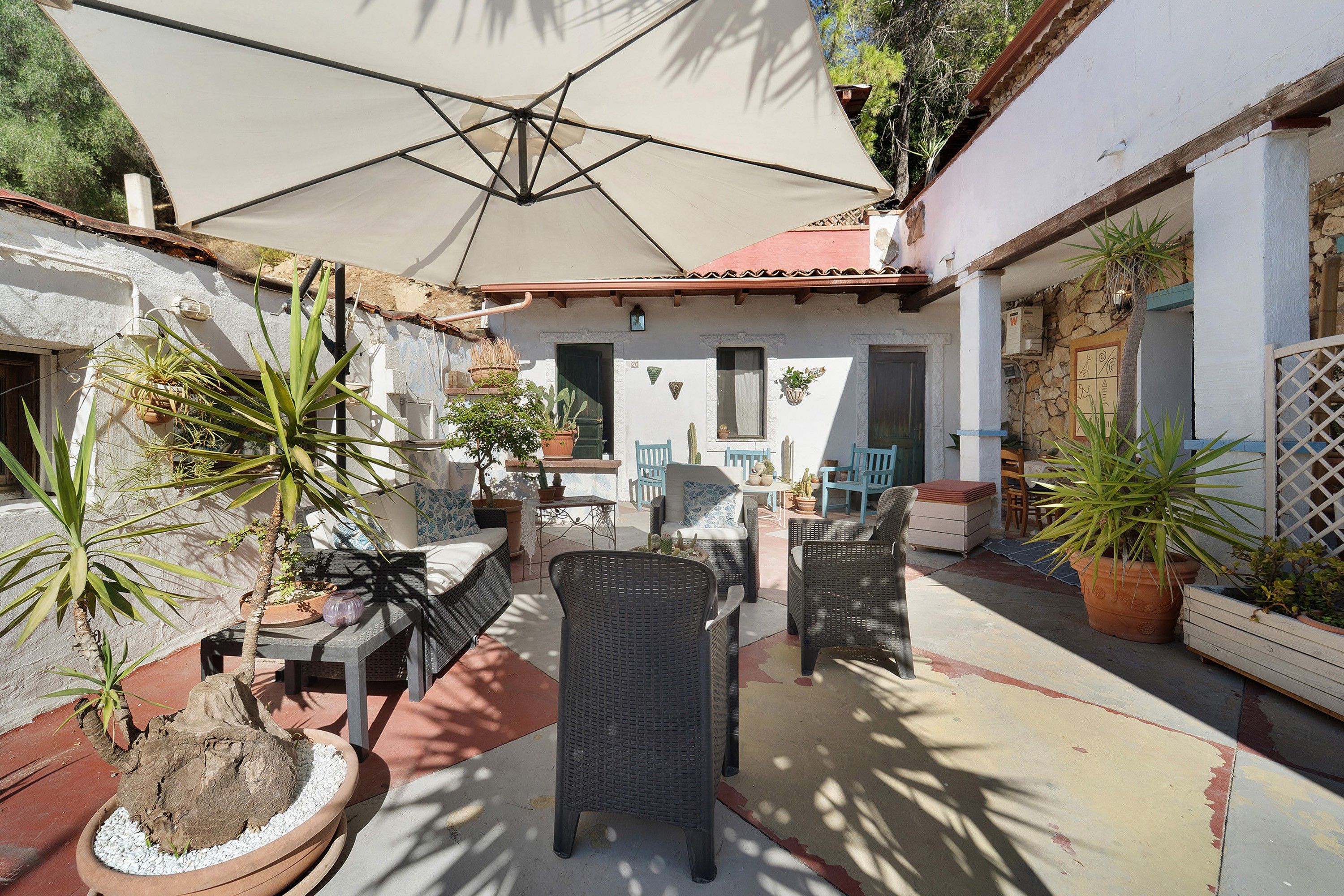 An outdoor patio area with a table and chairs, surrounded by potted plants and a large umbrella.