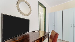 A room with a flat-screen TV on a wooden desk, a red chair, a decorative mirror, and a wardrobe. - Double room with shared pool and kitchen, Wi-Fi and air conditioning (Gonnesa)
