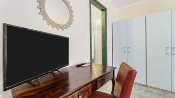 Une pièce comprenant un téléviseur à écran plat posé sur un bureau en bois, une chaise rouge, un miroir décoratif et une armoire.
