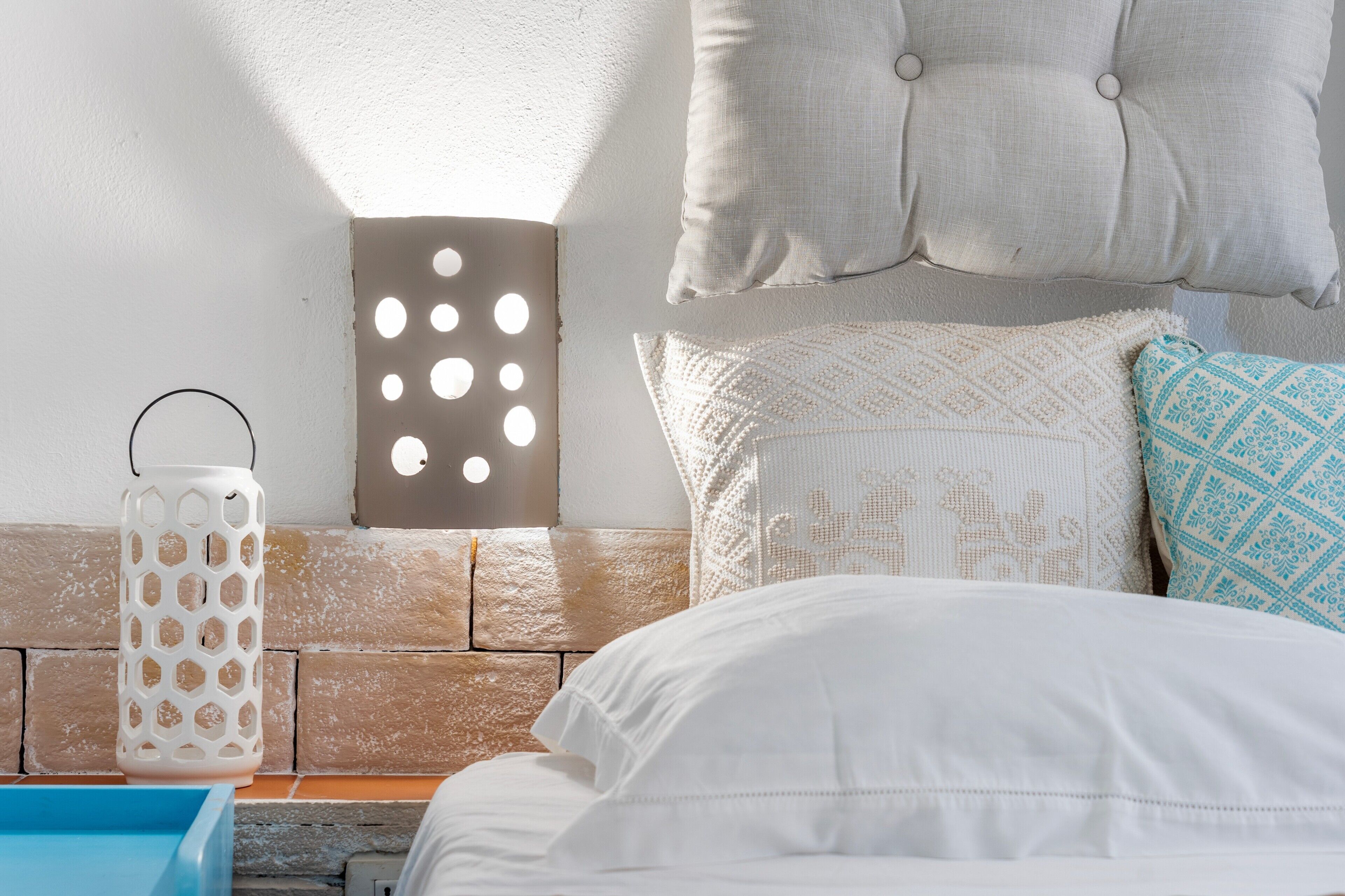 A bed with white bedding, a blue tray, a white lantern, and a wall with a textured pattern and a tufted pillow.
