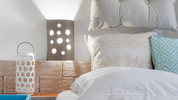 A bed with white bedding, a blue tray, a white lantern, and a wall with a textured pattern and a tufted pillow.