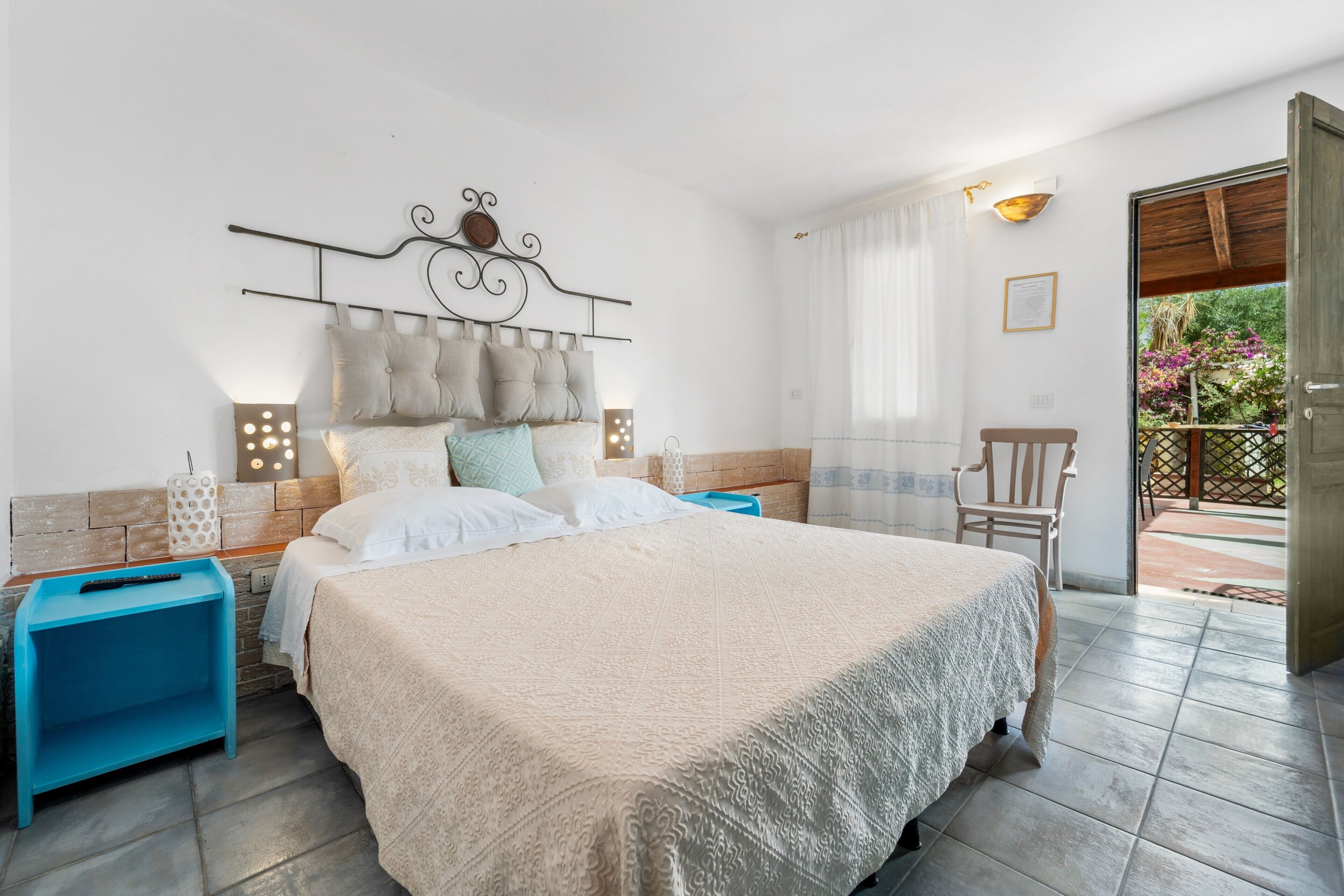 A bedroom with a bed, a nightstand, a chair, and a view of the outdoors.