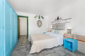 A bedroom with a bed, a blue wardrobe, a bedside table, a wall-mounted mirror, and a decorative wall piece. - Double room with shared pool and kitchen, Wi-Fi and air conditioning (Gonnesa)