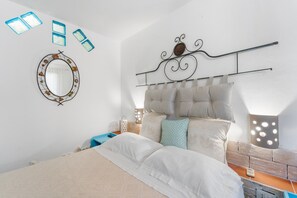 A bedroom with a bed, a headboard, a wall-mounted mirror, and a bedside table with a lamp.
