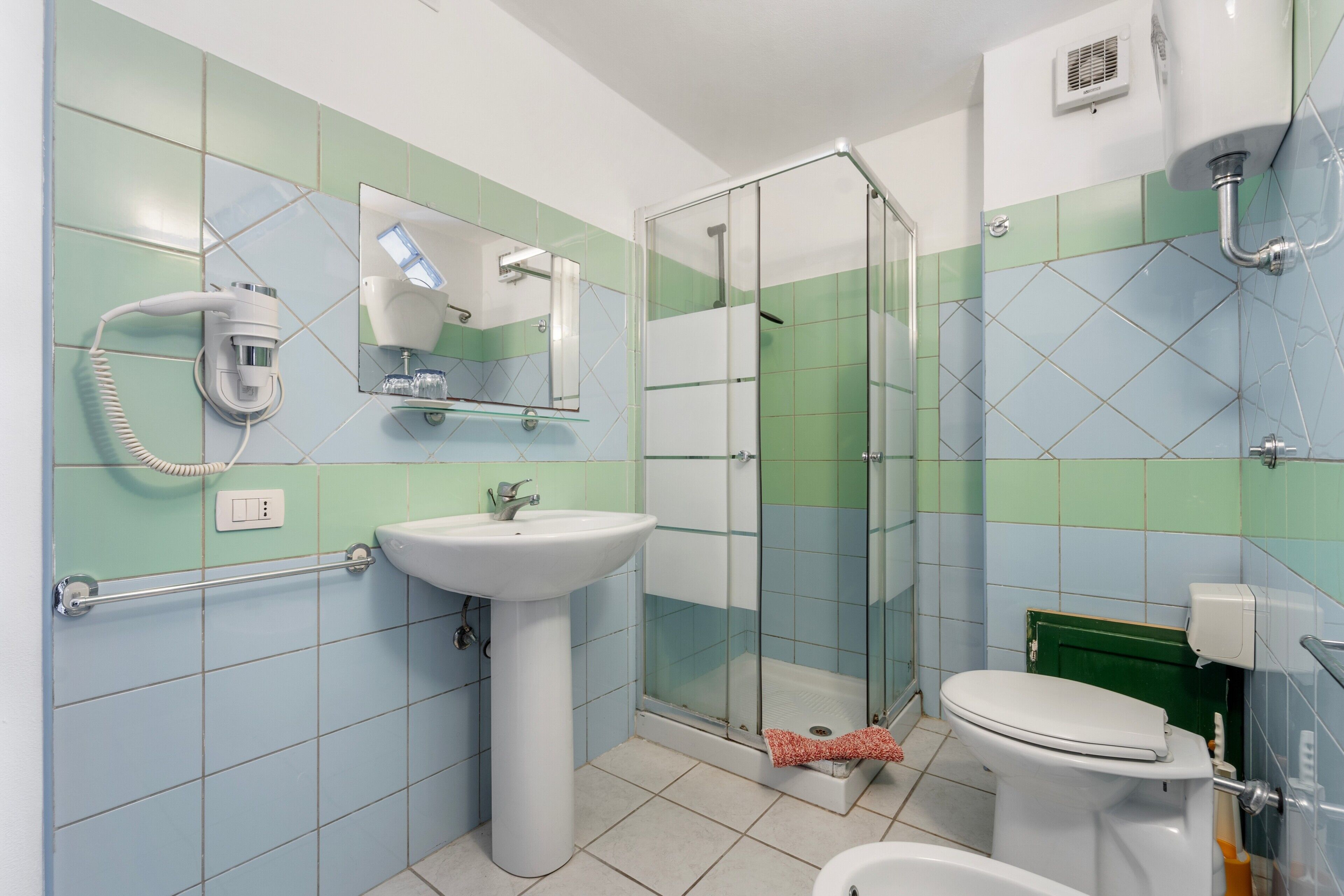 Un baño con cabina de ducha de vidrio, un lavamanos blanco, un inodoro y un espejo.