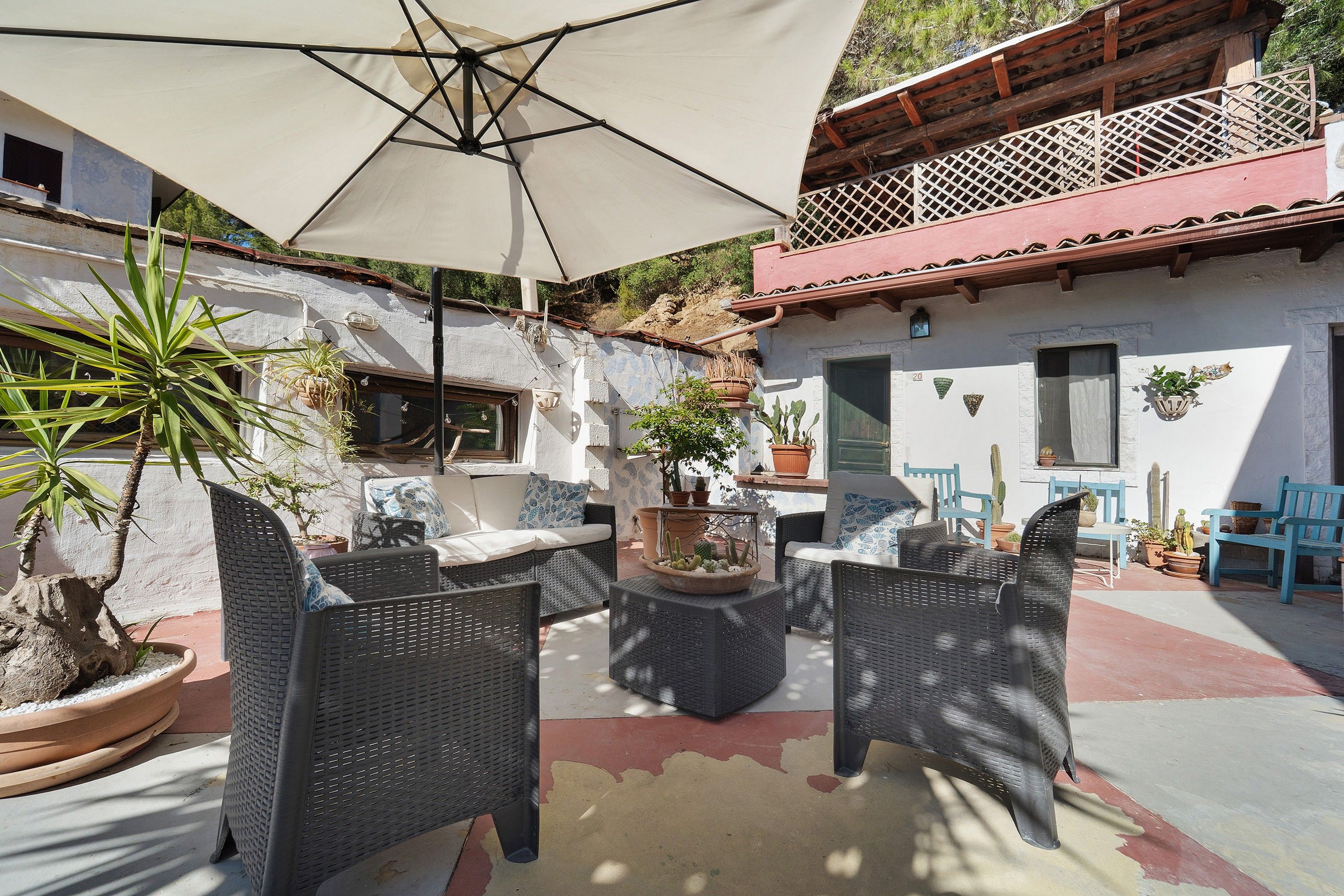 Een terras met rieten meubels, potplanten en een witte parasol.
