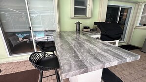 Eine Küche mit Marmorarbeitsplatte, einem Grill und einer Glasschiebetür, die auf eine Terrasse führt.