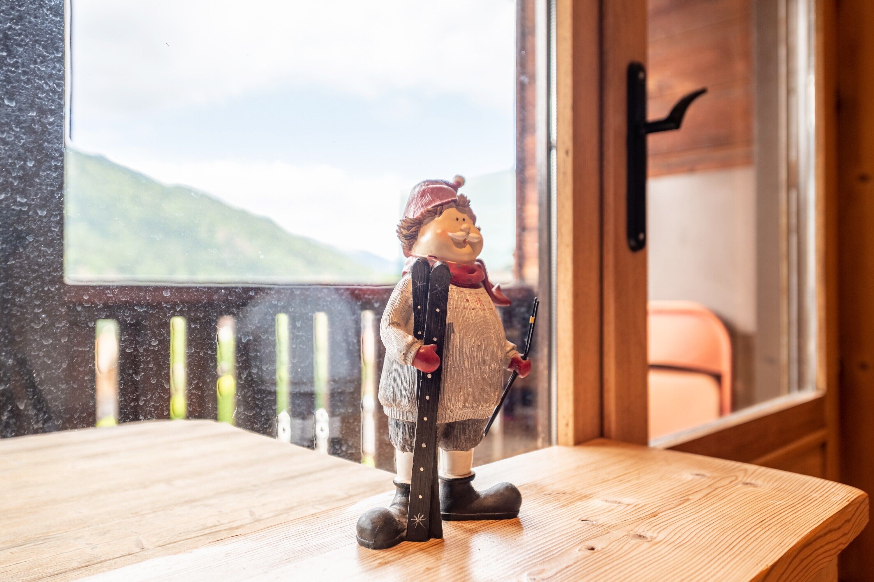 A figurine on a wooden table near a window with a view of a mountain.