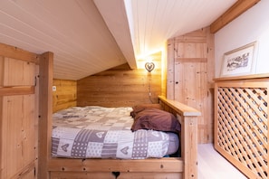 Ein hölzernes Etagenbett mit einer herzförmigen Leuchte darüber, eine Holzleiter und ein gerahmtes Bild an der Wand.
