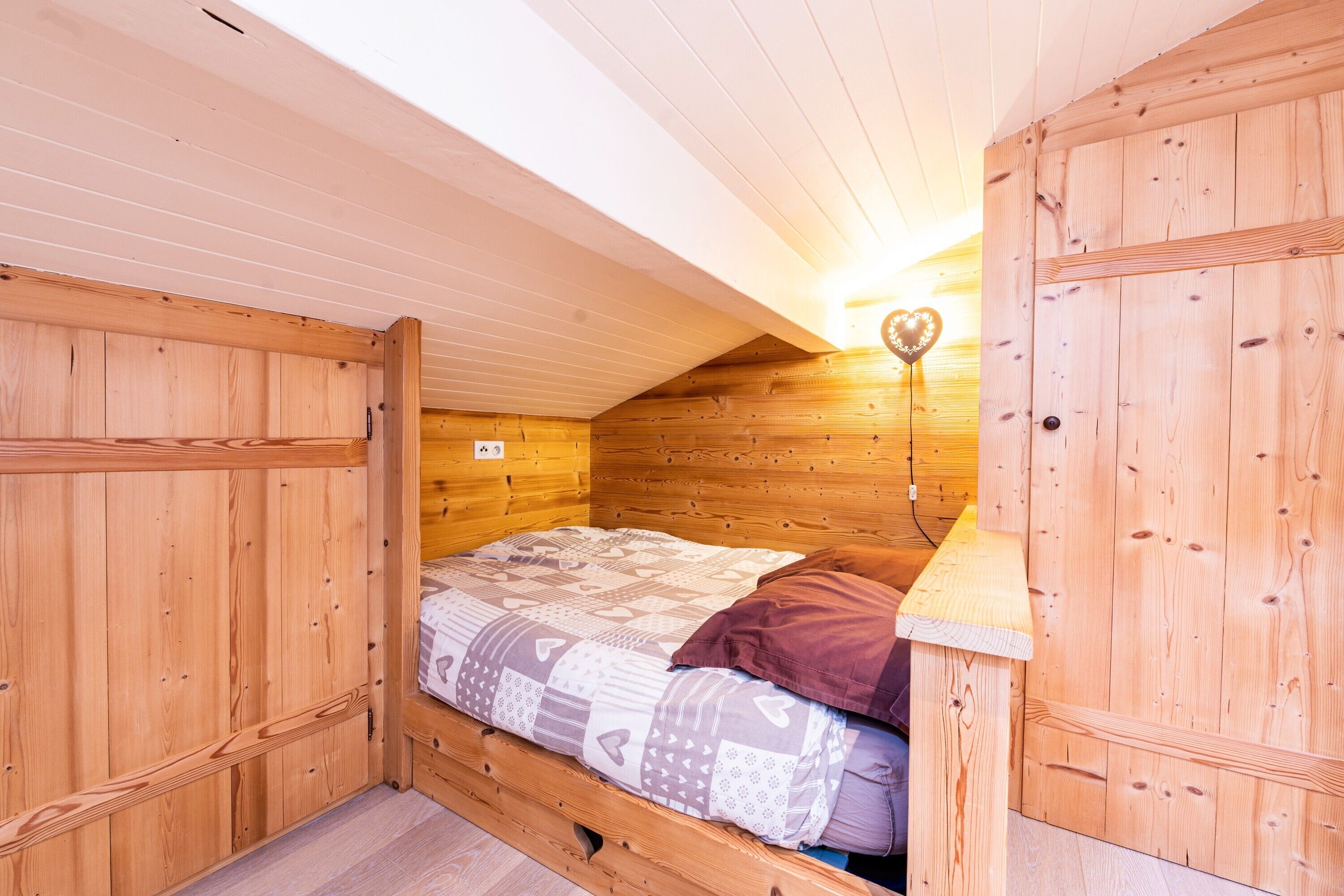 Ein Zimmer in einer Holzhütte mit einem Bett, einer Wandleuchte und einer lampenartigen Leuchte in Herzform.