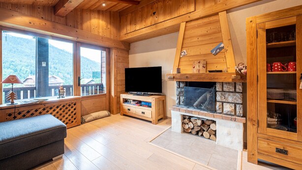 Un interior de madera con televisión, chimenea y ventanas amplias con vistas a la montaña.