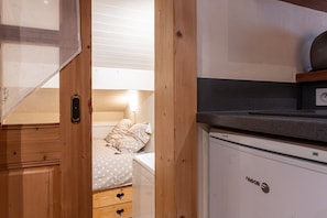 Une pièce de taille modeste comprenant un lit, une petite kitchenette et une porte en bois.