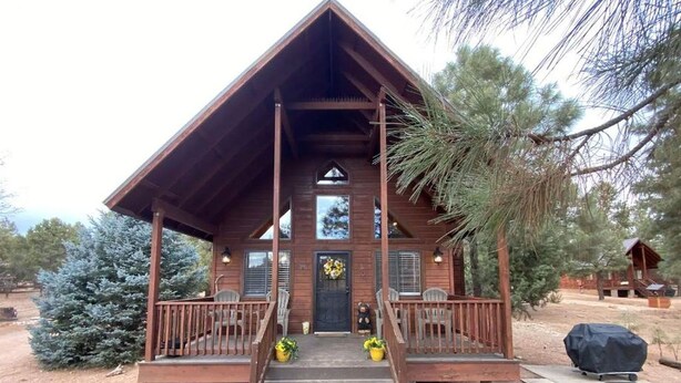 A wooden cabin with a porch, steps, and a covered area with a grill.