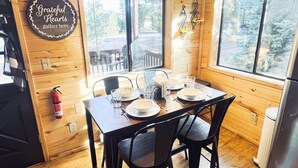 A wooden cabin dining area with a table set for four, a fire extinguisher, and a 'Grateful Hearts gather here' sign.