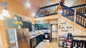 A cabin interior with a kitchen, dining area, and a staircase.